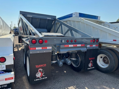Dump trailer showing Ranco LW21-40 logo and tandem axle with red taillights and protective mud flaps in a trailer yard.