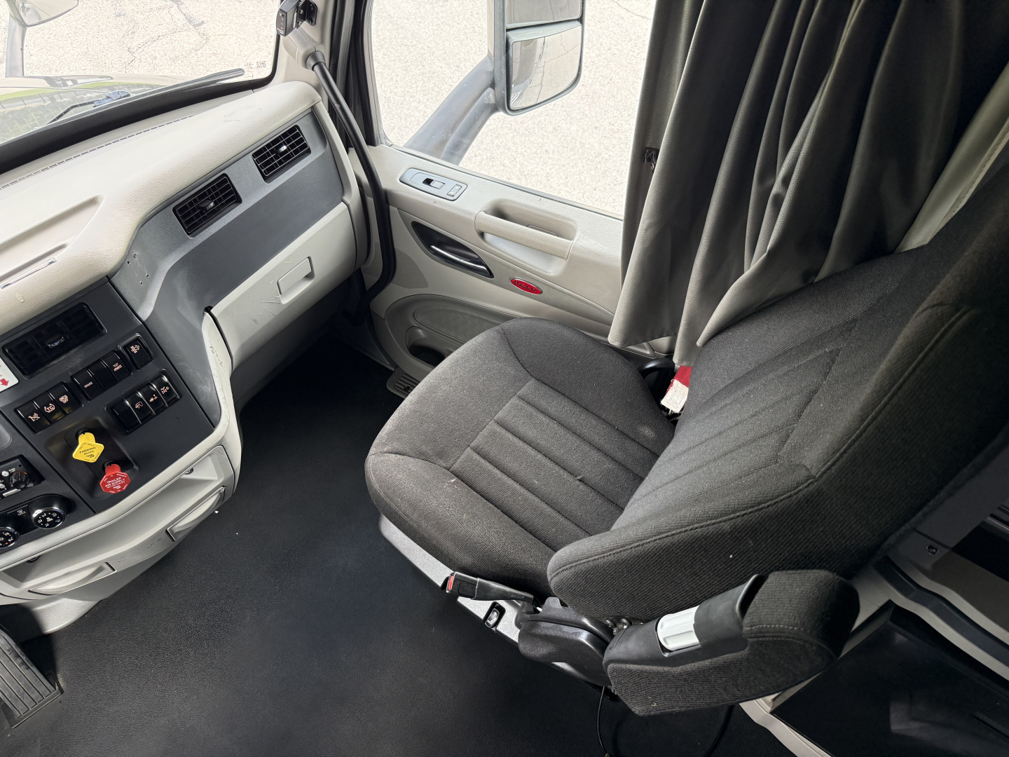 Peterbilt 579 cab interior showing gray dashboard, steering area, and driver's seat (armrest) in a sleeper truck cab.