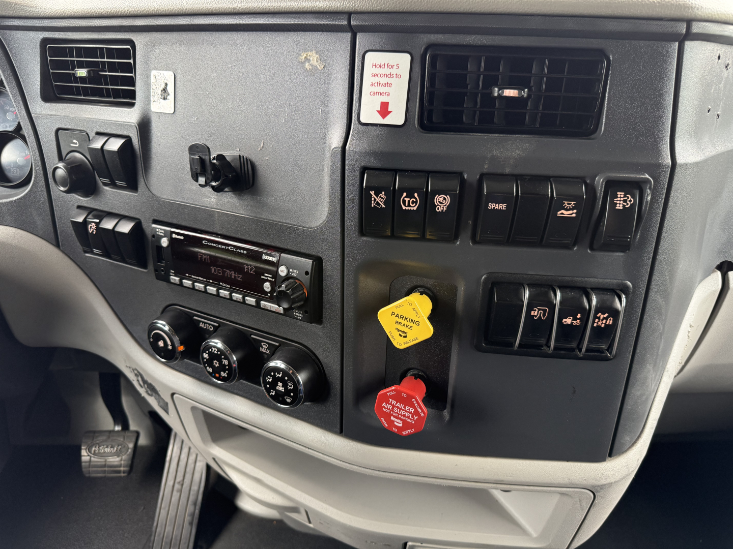 Peterbilt 579 dash panel with switches, knobs, and two colored knobs (yellow and red) in view; includes radio and climate controls.