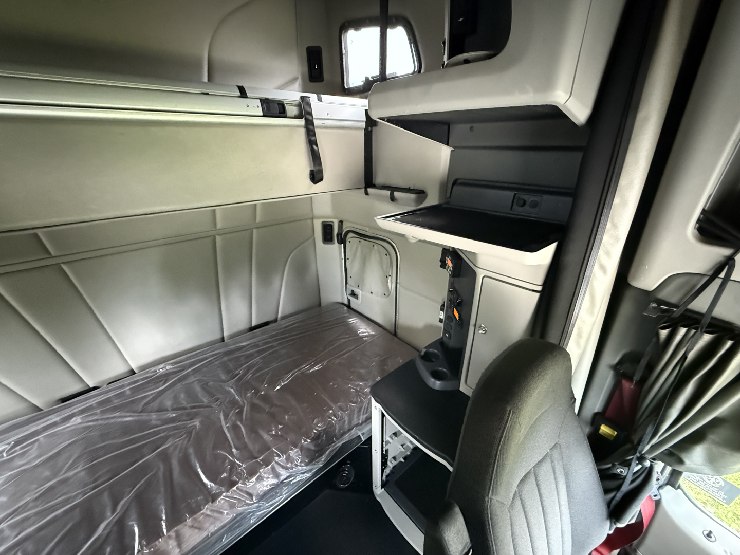 Peterbilt 579 sleeper cab interior showing bunk bed with plastic-wrapped mattress and cab storage shelves.