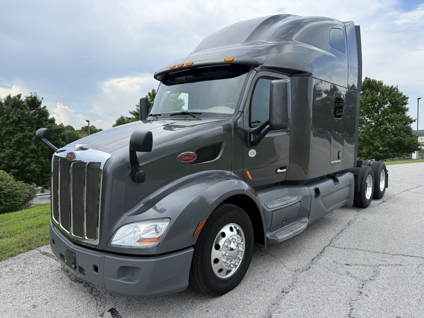 Peterbilt 579 sleeper cab tractor showing front grille with chrome surround, hood and headlights, side mirror, fuel tanks, and dual rear axles.