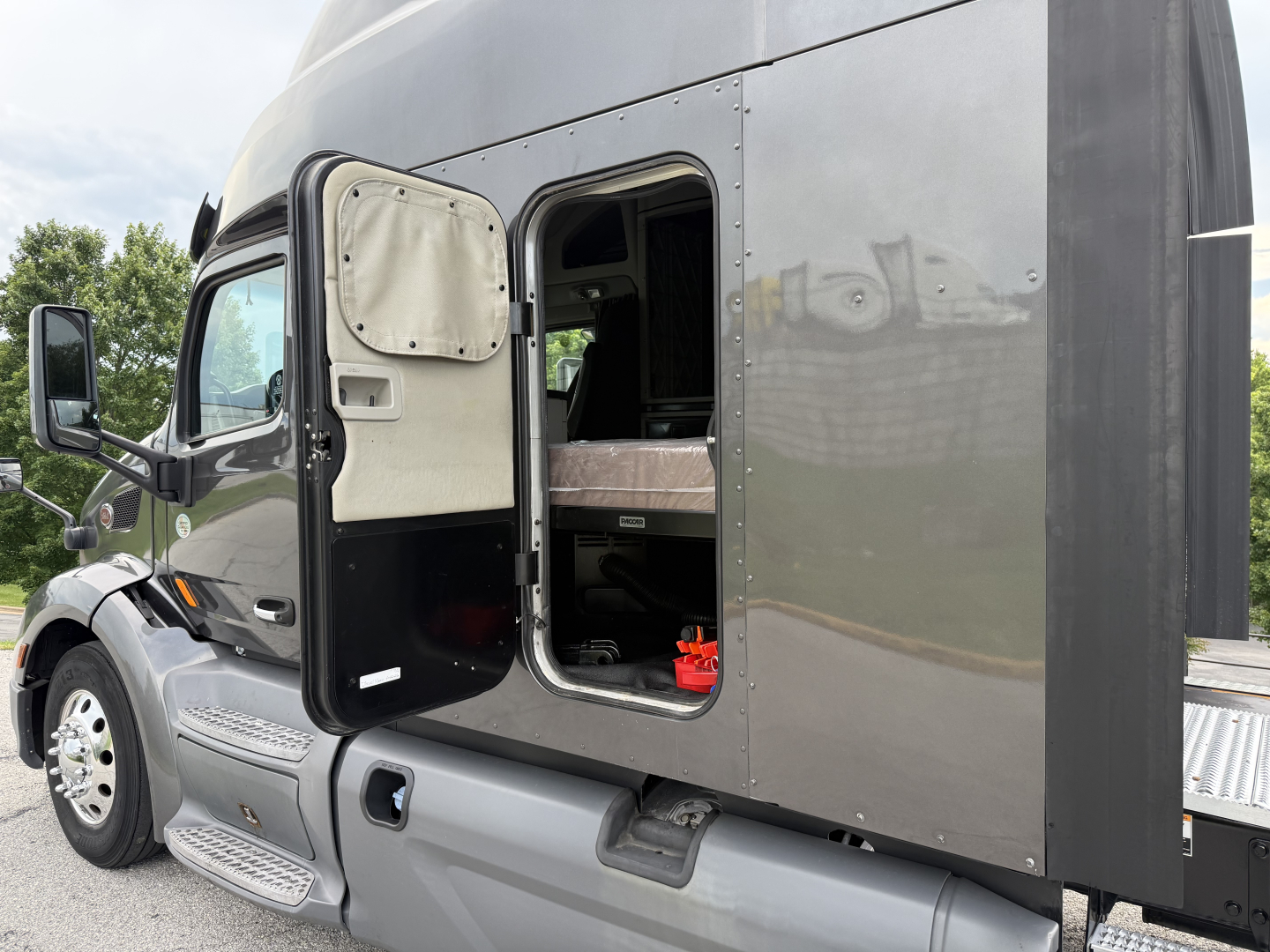 Peterbilt 579 truck cab door open showing sleeper area and side access panel; exterior gray paint and steps visible.