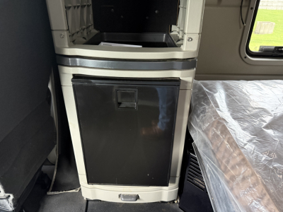 Panel and cabinet area inside a Peterbilt 579 cab showing a black vertical storage cabinet door and surrounding light gray panels with a silver trim.