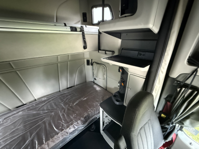 Peterbilt 579 sleeper cab interior showing bunk bed with plastic-wrapped mattress and cab storage shelves.