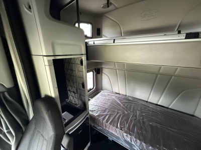 Peterbilt 579 sleeper cab interior showing a bunk bed with plastic cover, storage compartments, and light gray panels.