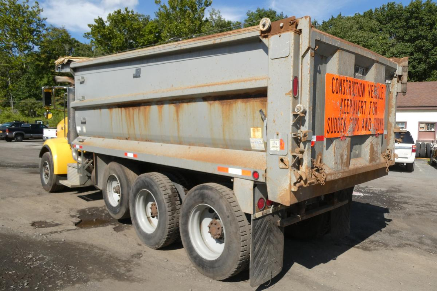Dump truck bed of a 2005 Peterbilt 357 dump truck with rusted metal sides, orange warning sign on rear, and dual rear axles.