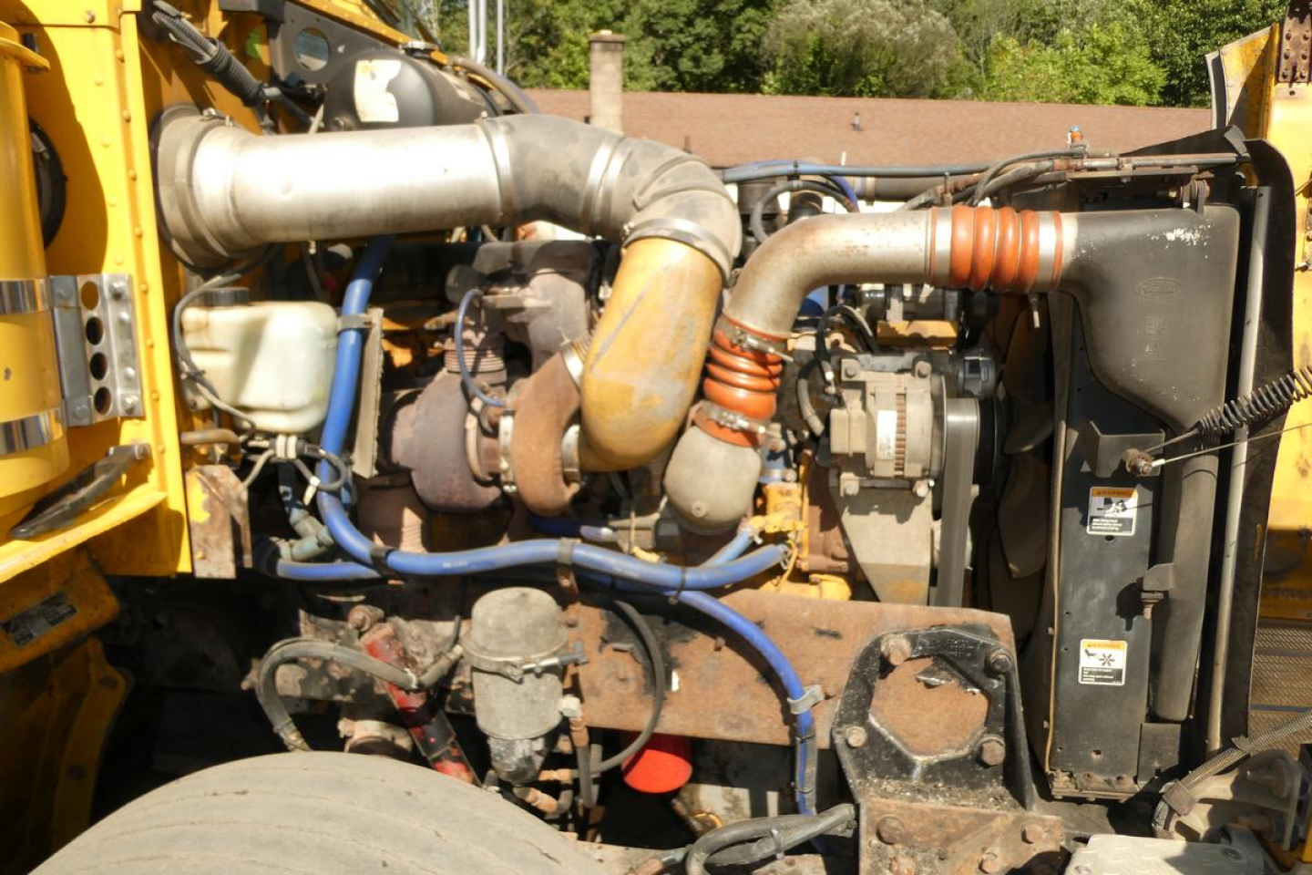 Peterbilt truck engine bay showing large exhaust manifold, blue hoses, coolant reservoir, and radiator with fans.