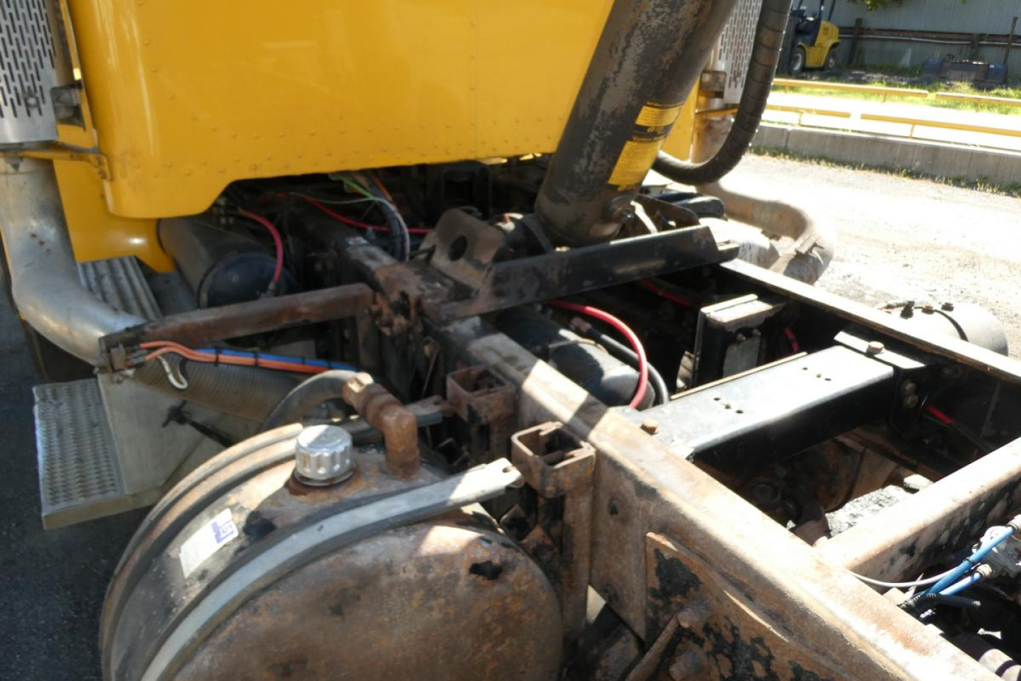 Dump truck engine bay showing fuel tank, hydraulic lines, and chassis with exposed frame rails in view.