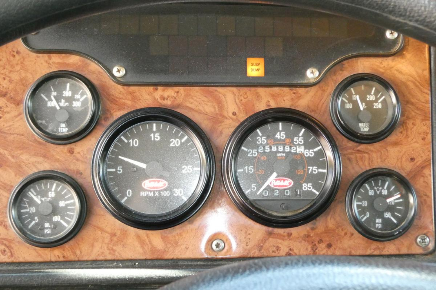 Peterbilt truck dashboard with multiple gauges and woodgrain panel; center tachometer and speedometer readings visible