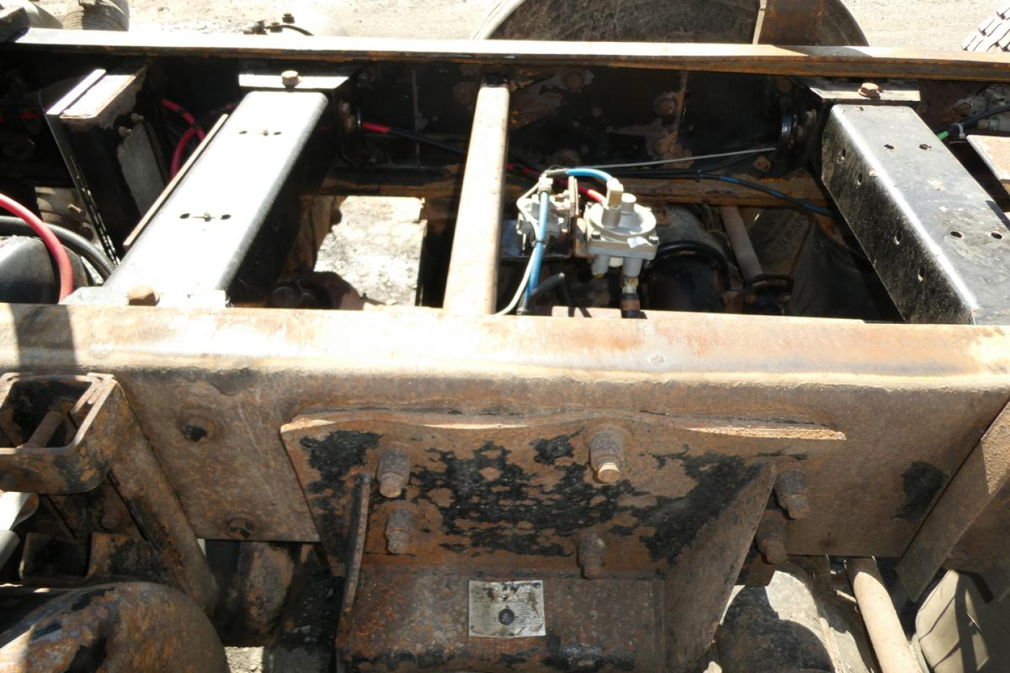 Dump truck frame with engine bay components and rusted chassis showing wiring and a small device mounted between rails.
