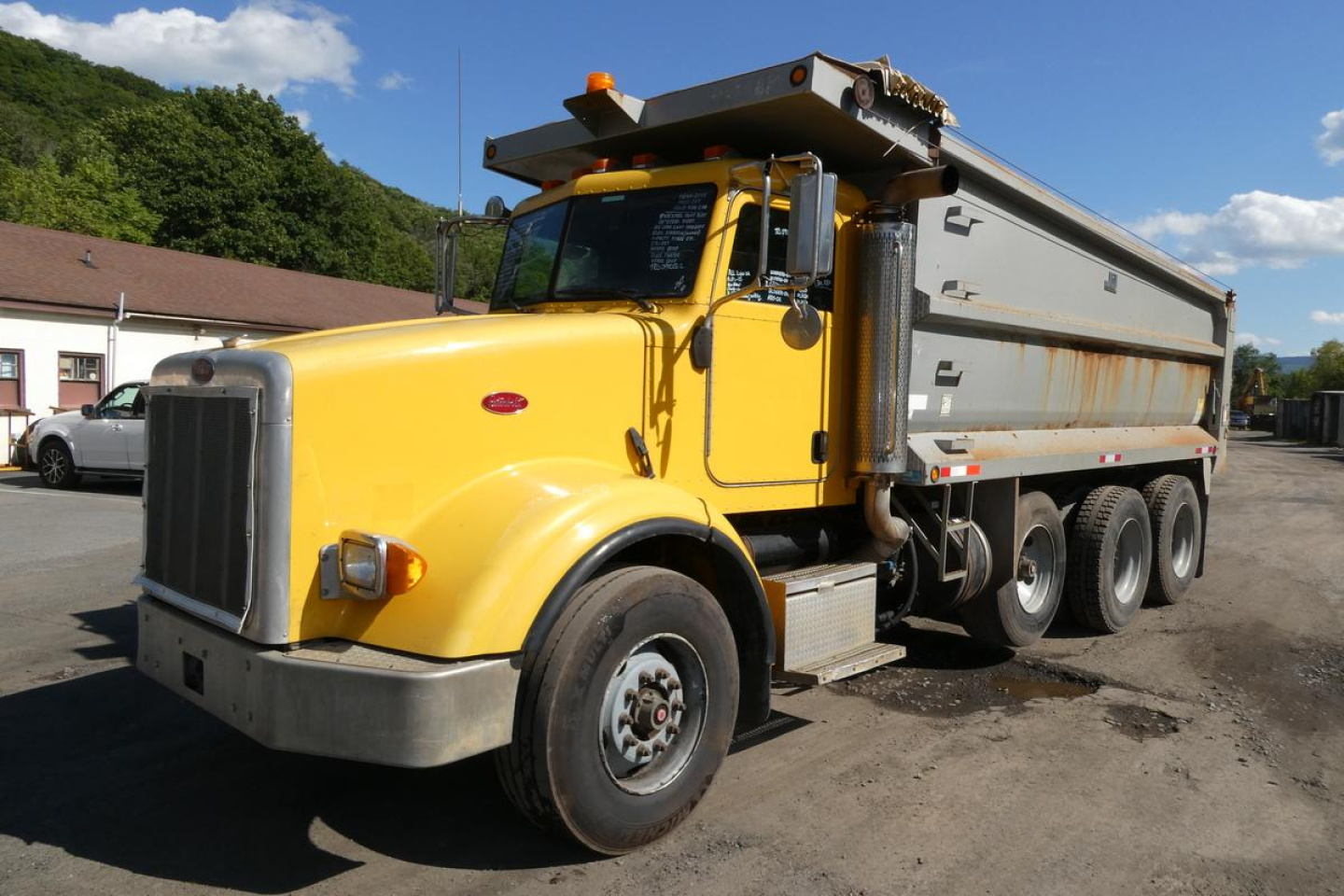Dump semi-truck chassis and yellow Peterbilt 357 dump bed viewed from front-left side showing large grille, dual rear axles, and raised dump body.