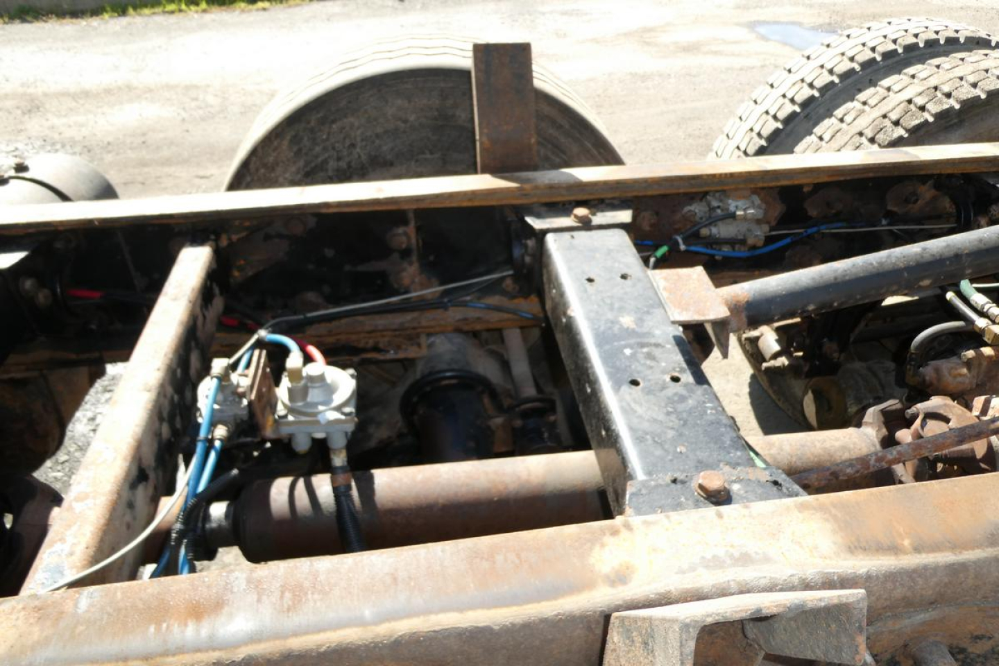 Truck chassis with exposed drivetrain components and rusted frame from a Peterbilt 357 dump truck; visible hoses, wiring, and partial suspension elements.