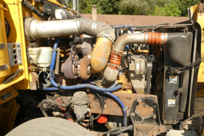 Peterbilt truck engine bay showing large exhaust manifold, blue hoses, coolant reservoir, and radiator with fans.