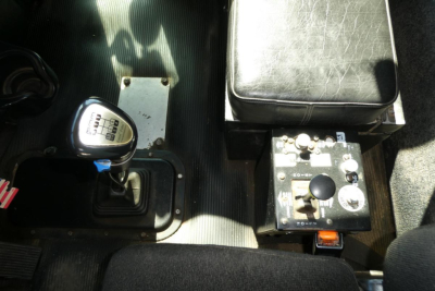 Truck cab interior with gear shifter and control panel showing a square metal box and toggles.