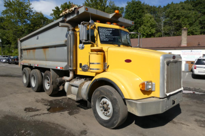 Peterbilt dump truck 2005 model with yellow cab and gray dump bed parked outdoors; view shows front-left side with wheel, headlights, and orange warning light on cab.
