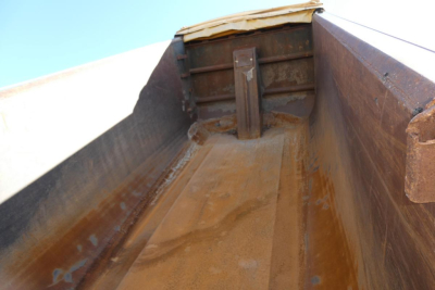 Truck bed interior of a Peterbilt 357 dump truck showing rusted metal bed with side walls and tailgate hinge.