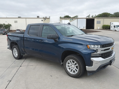 Chevrolet Silverado 1500 LT Crew Cab 4x4 pickup truck in blue, front-right view, visible badges and chrome bumper; Silverado badge on fender; cargo bed, wheels, and dealership lot backdrop.