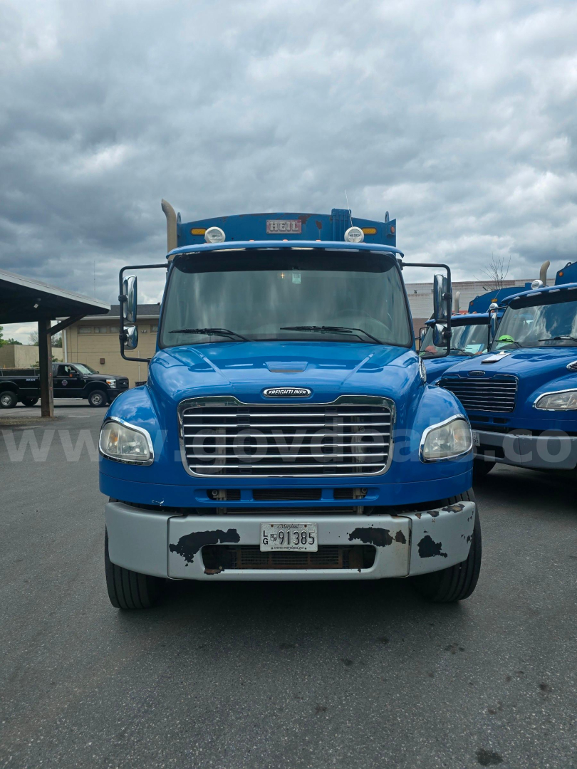 Front view of a blue 2012 Freightliner M2 106 truck with grill, headlights, and front bumper showing some paint wear and California license plate.