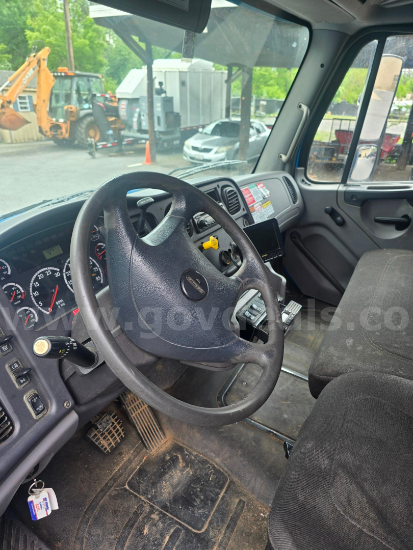 Freightliner M2 106 truck interior showing steering wheel and dashboard with gauges.