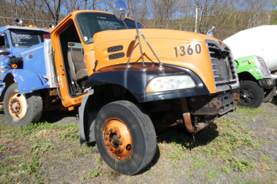 Front-right view of a yellow and black 2004 Mack CX612 conventional daycab truck, number 1360, with exposed front axle and large front tire, VIN plate and stock number nearby.