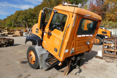 Truck cab of a 2004 Mack CX612 with orange exterior rotated on single front wheel and visible wheels, side mirrors, and cab components.
