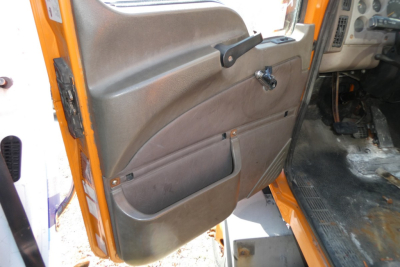 Door panel of a Mack CX612 truck showing brown plastic interior with pocket, window crank, and armrest; part of orange exterior visible.