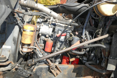 Engine bay showing fuel filter, hydraulic lines, wiring, and a red battery near a Mack CX interior components