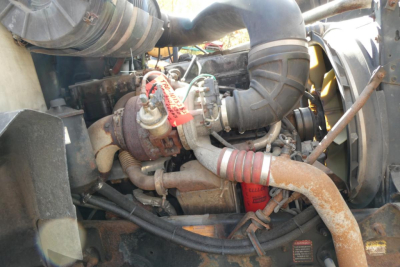Mack CX612 engine bay showing turbocharger, intake piping, and hoses with red tag on hydraulic line.