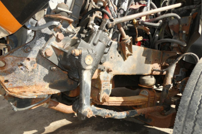 Truck front suspension and steering components with Rust and wear visible on frame; diesel drivetrain with hoses and fittings in view.
