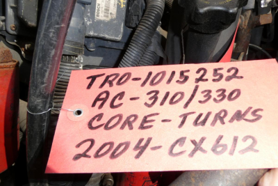 Tag showing handwritten stock and model notes: 'TR0-1015252 AC-310/330 CORE-TURNS 2004-CX612' attached to vehicle engine area.