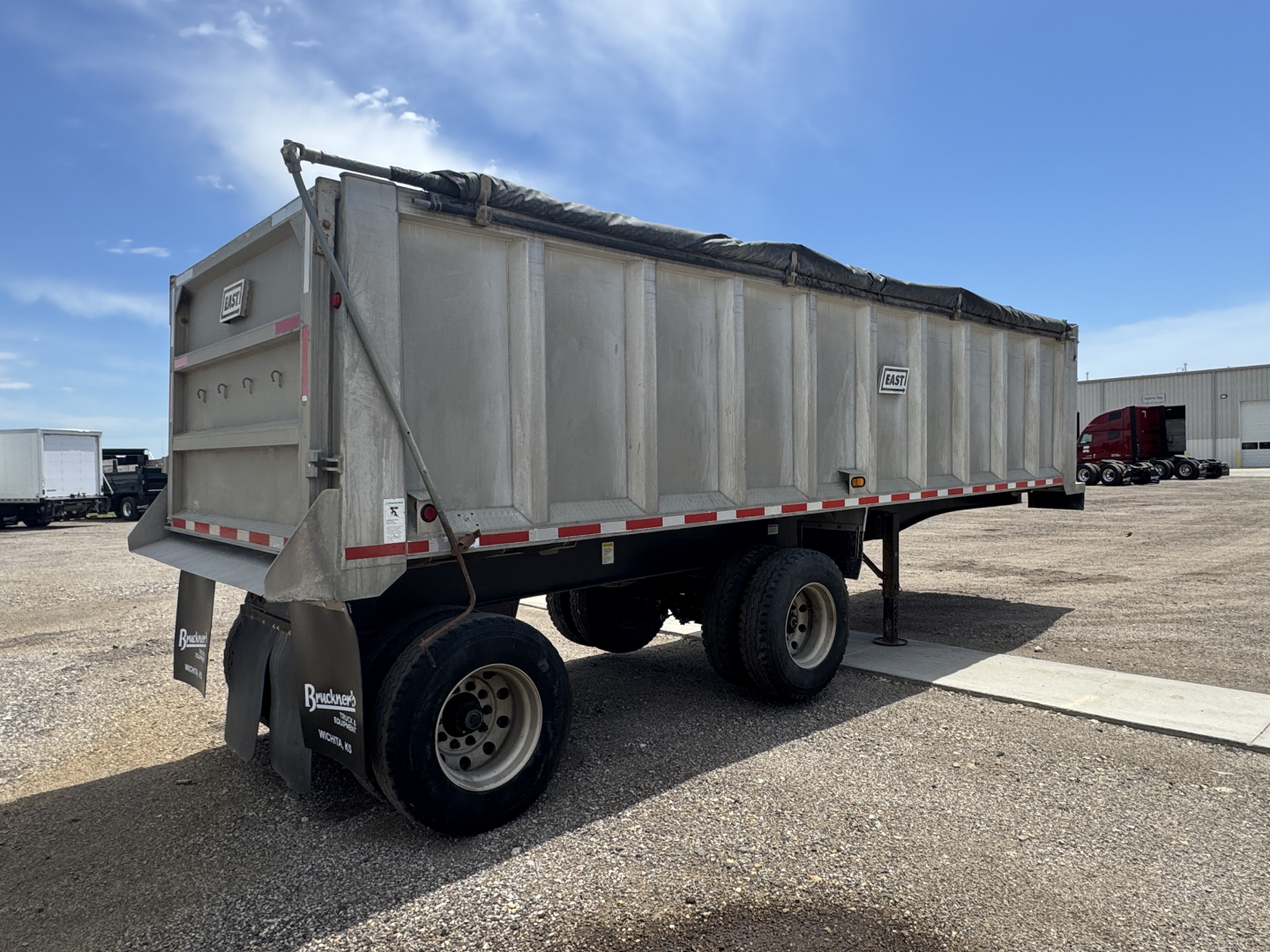 Dump trailer in side view showing Weathered metal cargo area with rear doors, dual axles, and mud flaps.