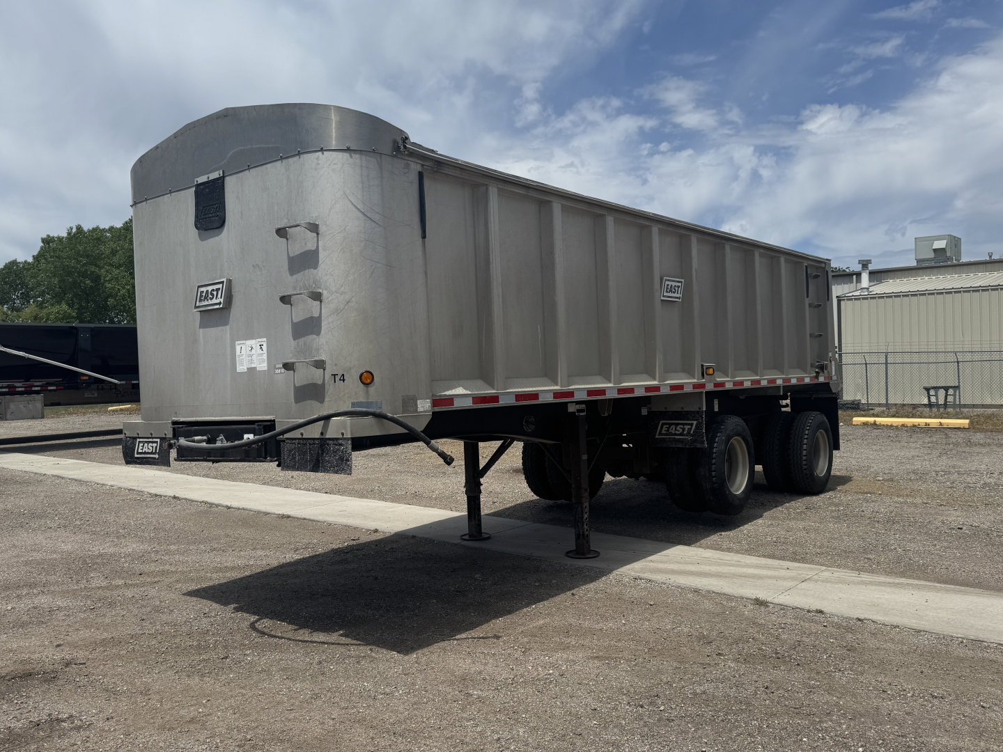 Dump trailer in side view showing metal body and dual rear axles with a front support leg extended.