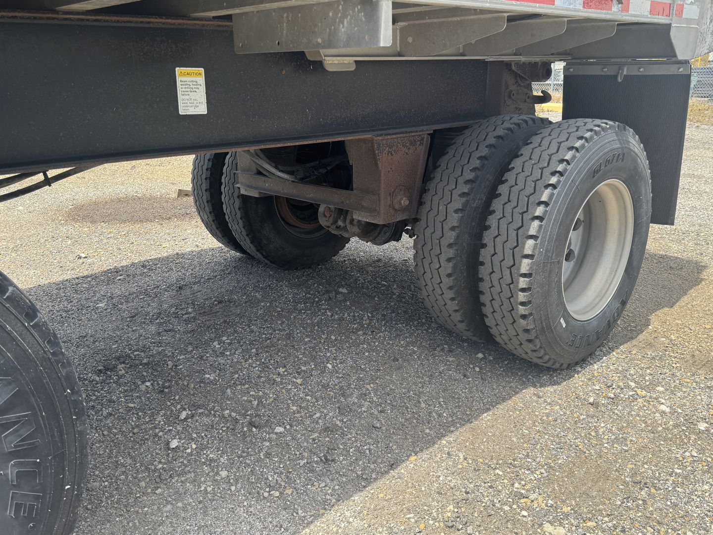 Trailer undercarriage showing dual rear tires and suspension components of a dump trailer.
