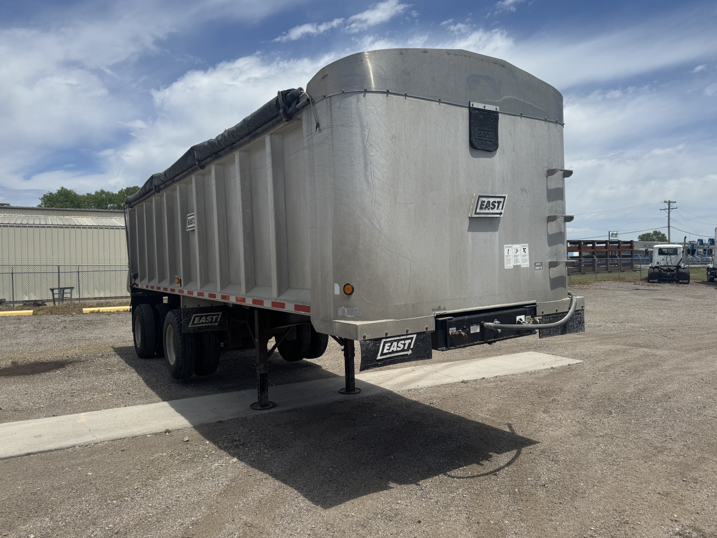 Dump trailer from side and rear view showing aluminum body, black undercarriage, two axles, and front landing gear. East brand plate visible.