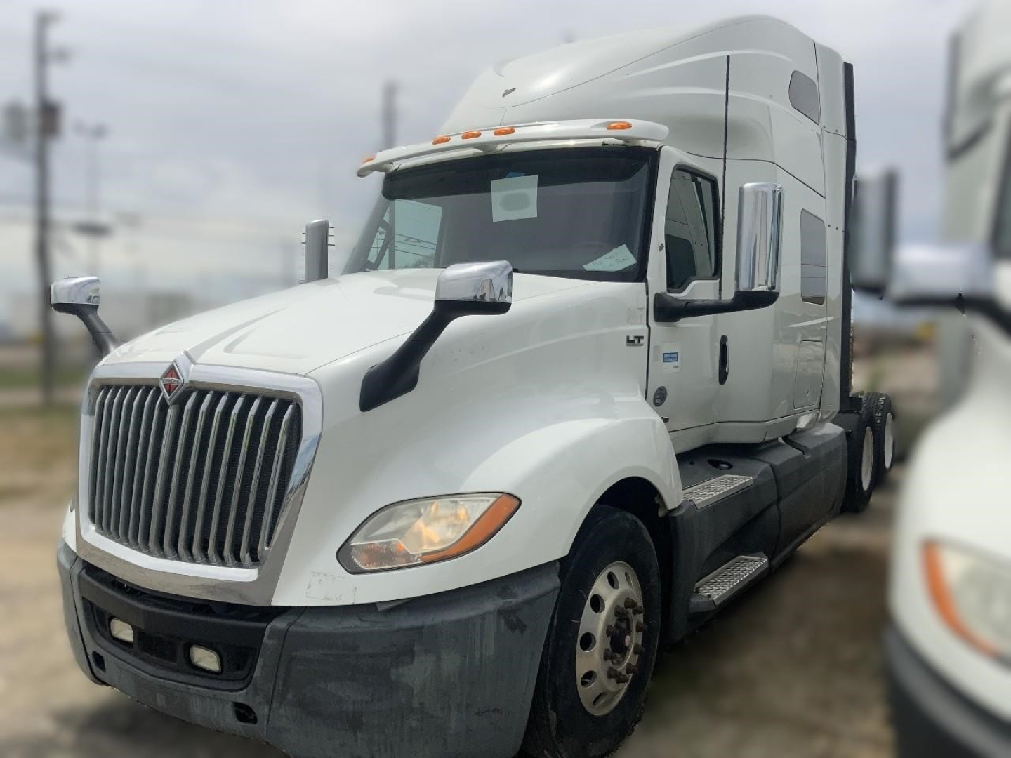 Truck cab in a white 2018 International LT conventional sleeper tractor, front-left angle, with chrome grille, large mirrors, and dual rear axles; VIN tag not visible.