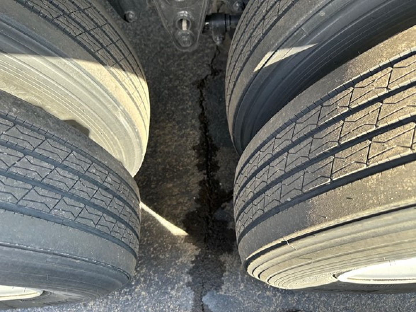 Flatbed trailer tires and suspension area showing dual axles and tires with tread pattern visible.
