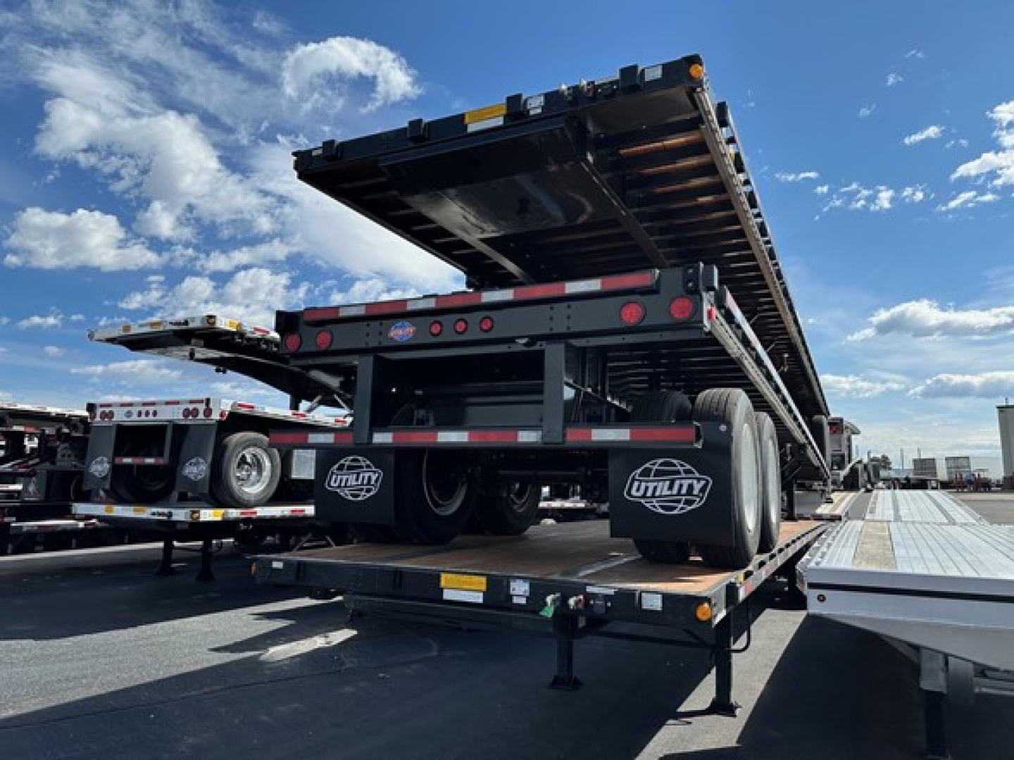 Utility 4000S flatbed trailer on a tow truck bed with raised deck, rear view showing tandem axles and reflective strips.
