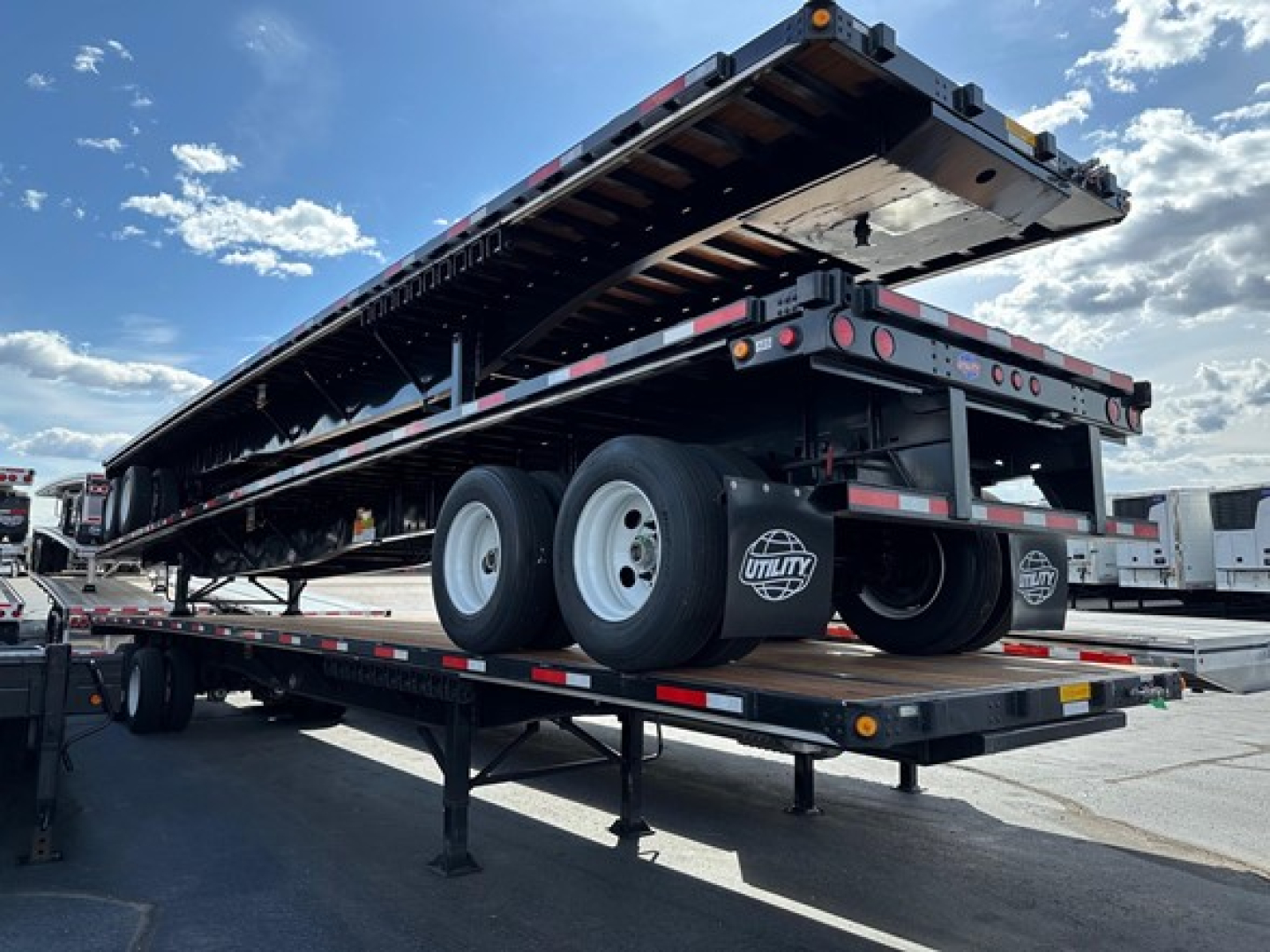 Flatbed trailer stacked on a trailer with dual rear axles and spare tires visible, Utility 4000S model, new condition, outdoor lot.