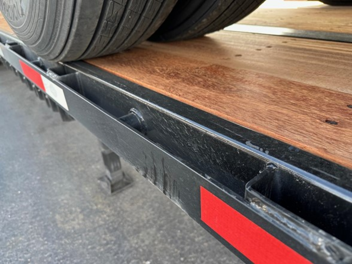 Plateau-style flatbed trailer deck with wooden planks and dual tires, side rails, and reflective red/white tape visible.