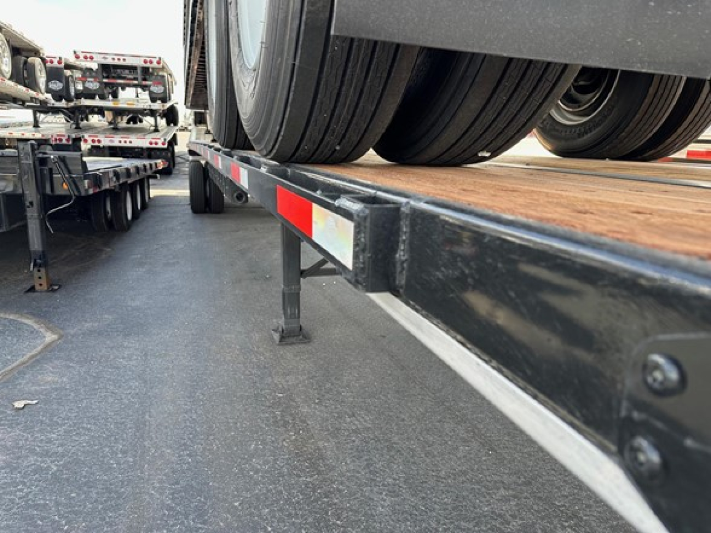 Flatbed trailer deck and dual rear tires of a Utility 4000S seen from side angle showing wheel, frame, and reflective safety strip.
