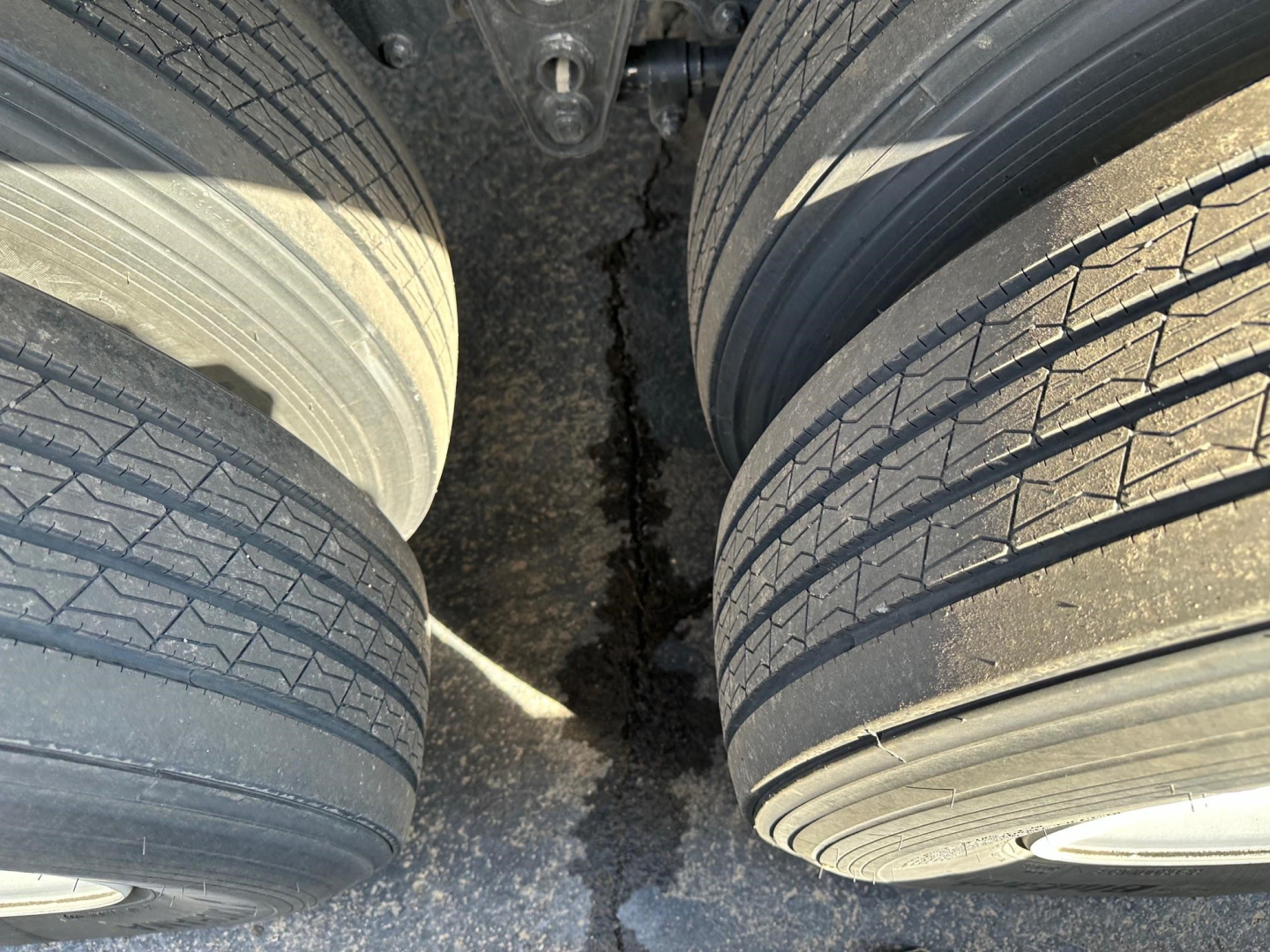 Trailer axle area with dual wheels, tread detail on tires, and gap between tires showing dark asphalt surface.