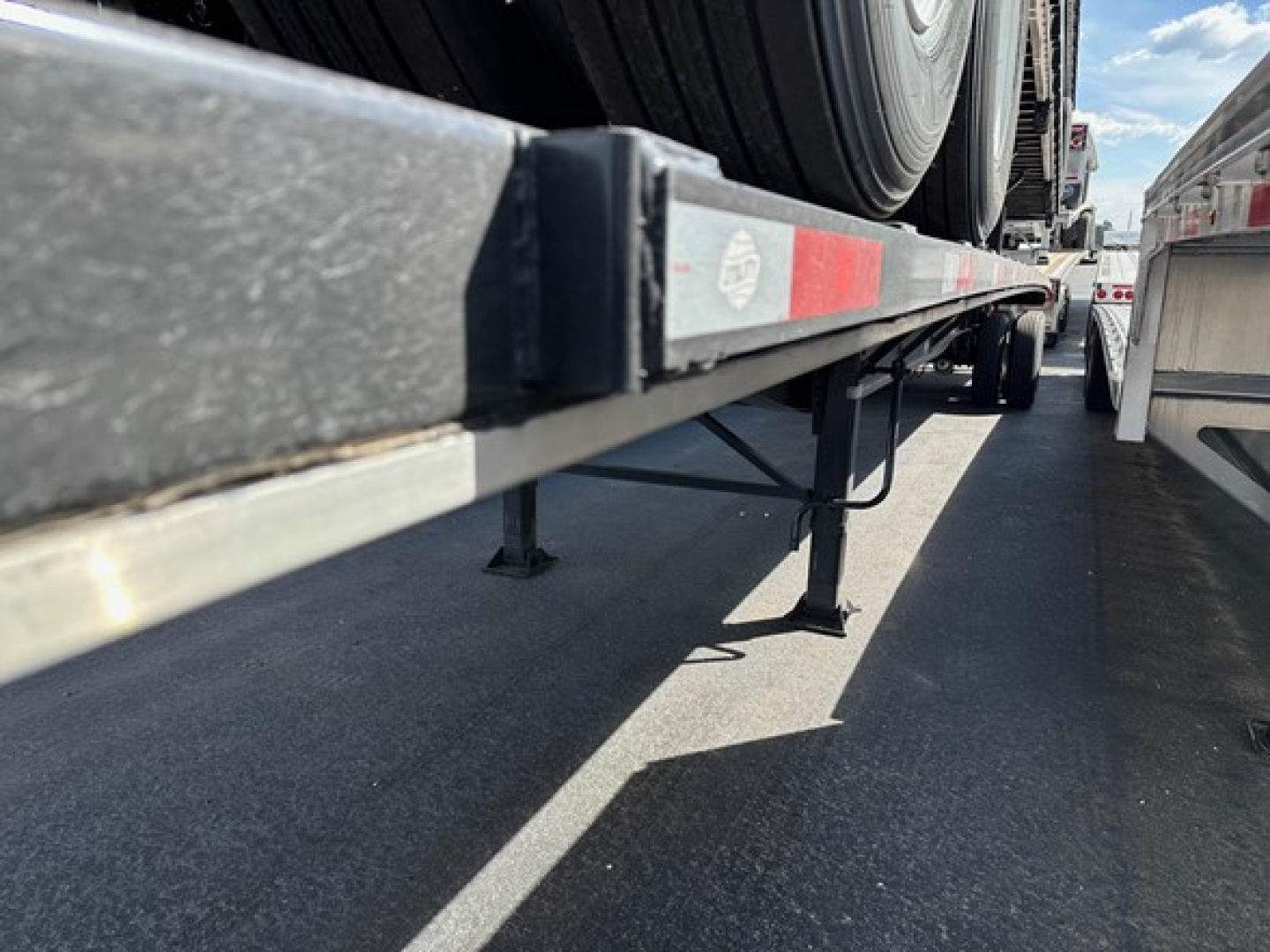 Trailer undercarriage with dual tires on a flatbed trailer showing support stands and reflective strip along railing.