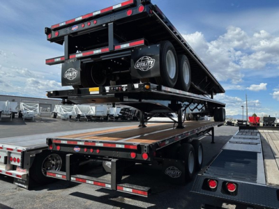 Flatbed trailer stacked on a carrier trailer with Utility branding, dual rear tires, and reflective safety markings.