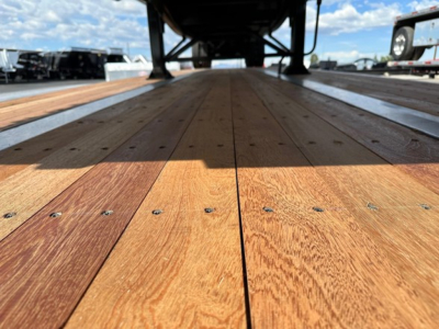 Flatbed trailer bed with wooden planks and hardware, undercarriage visible at far end, labeled as new Utility 4000S trailer.