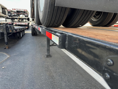 Flatbed trailer deck with dual rear tires and metal framework; low-angle view from side showing wheel, deck surface, and underside details.