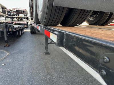 Flatbed trailer deck and dual rear tires of a Utility 4000S seen from side angle showing wheel, frame, and reflective safety strip.