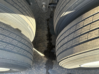 Trailer axle area with dual wheels, tread detail on tires, and gap between tires showing dark asphalt surface.