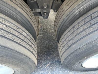 Trailer axles and tires view showing dual tandem wheels with tread pattern and hub caps, part of a flatbed trailer undercarriage.
