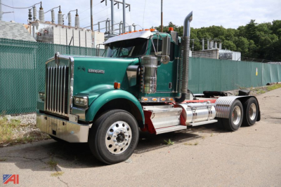 Kenworth W900 truck tractor in green with chrome fuel tanks and exhaust stacks, 2011 model, conventional daycab, three rear axles, on paved lot.