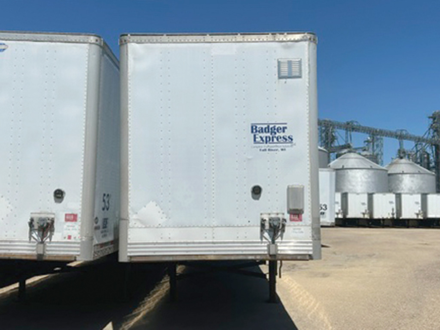 Trailer rear view showing Badger Express logo on a white cargo trailer with support legs and ramp doors, other trailers in background.